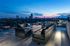 Outdoor lounge area with a long grey and blue couch and chairs seated around a rectangle table with a firepit on top. There are glass walls overlooking the skyline.