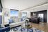 apartment living area with sofa and arm chair seating area next to kitchen with counterheight island with, stainless steel appliances and dark wood toned cabinets