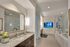 large bathroom with two separate sinks and framed mirrors, soaking tub and frameless glass shower with inlaid TV on the wall next to shower