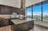 kitchen with wall of large windows, island with range and stainless steel and glass venthood, brown wood-tone cabinets, granite counters with coordinating white tile backsplash