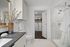 Bathroom with toilet, frameless glass shower with white marble tile and vanity area with white wood cabinetry and black stone counters