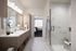 apartment bathroom with glass frameless shower, vanity with one sink and framed mirror