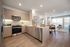 apartment kitchen with light wood cabinets, stone counters and backsplash, with dining and living area behind
