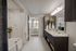 en suite bathroom with single vanity with storage below, framed mirror, and soaking tub with tile surround