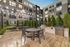 Modern outdoor communal area with elegant lighting, featuring a stylish dining setup, BBQ grills, and a lush garden setting in a contemporary apartment complex.