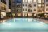 Luxurious apartment complex featuring a beautifully illuminated swimming pool surrounded by elegant lounge chairs and modern architecture.