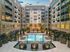 Luxurious apartment complex courtyard featuring a sparkling pool, elegant outdoor seating, and lush greenery at sunset.