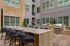 Elegant outdoor communal area featuring a modern dining setup with sleek bar stools, stylish granite countertop, and built-in stainless steel grills, surrounded by a sophisticated apartment building façade.