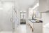 Elegant bathroom featuring a luxurious shower, plush white robe, and modern vanity with stylish decor, leading to a cozy bedroom with natural light.