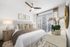 Bright and elegant bedroom featuring a plush bed with patterned pillows, modern ceiling fan, and expansive window with stylish blinds.