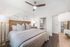 Bright and elegant bedroom featuring a plush king-sized bed with stylish decorative pillows, modern ceiling fan, chic wall art, and a glimpse into the en-suite bathroom.