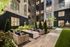 Elegant courtyard in a modern apartment complex featuring cozy seating around a sleek outdoor fire pit, surrounded by lush greenery and well-lit windows.