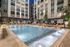 Luxurious apartment complex with a beautifully illuminated pool, surrounded by modern architecture and lush greenery, perfect for a relaxing evening swim.