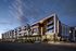 Modern apartment complex at dusk with illuminated facade, stylish balconies, and spacious parking area.