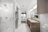 Elegant modern bathroom with dual sinks, sleek wood cabinetry, and a spacious shower, leading into a bright bedroom with a large window.