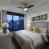 Elegant bedroom with city skyline view, featuring a plush bed adorned with decorative pillows and modern art on the walls, accentuated by warm lighting and contemporary furnishings.