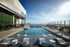 Luxurious rooftop pool with modern lounge chairs, elegant hanging basket chairs, and breathtaking city views under a clear blue sky.