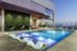 Luxurious rooftop pool area with modern lounge chairs, hanging egg chairs, and a stunning city view at twilight.