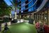 Luxurious apartment exterior with lush landscaped garden, modern glass facade, and well-lit palm trees.