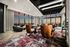 Luxurious living room with panoramic city views, featuring elegant leather chairs, modern decor, and a vibrant patterned rug, bathed in sunset hues.
