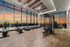 Luxurious fitness center with state-of-the-art equipment and stunning city sunset views through floor-to-ceiling windows.