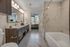 Luxurious bathroom with elegant marble tiles, sleek double vanity, and modern lighting; view of the cozy bedroom with a cityscape backdrop.