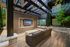 Modern outdoor lounge area with sleek design, featuring a plush sofa, wall-mounted TV, and stylish pergola.