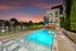 Luxurious evening poolside view with modern apartment building, elegant lounge chairs, and vibrant sunset backdrop.