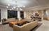 Luxurious open-concept living area with modern leather sofas, elegant chandelier, and a sleek kitchen with a large island and bar seating.