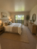 Serene bedroom with cozy beige decor, large window for natural light, and lush greenery view.