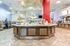 Modern cafeteria with a central serving counter, vibrant red pillar, and stylish tiled flooring.
