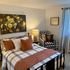 Inviting bedroom with plaid bedding, floral artwork, and a charming armchair for relaxation.