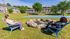 Residents enjoying a sunny day outdoors by a stone fire pit with a basketball court in the background.