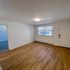Inviting living room with wooden flooring, large window, and access to an adjoining carpeted room.