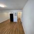 Bright and open apartment with wood flooring, modern lighting, and a sleek black refrigerator.