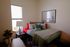 Cozy bedroom with stylish decor, featuring a plush bed adorned with colorful pillows, a modern lamp, large artwork, and abundant natural light.