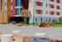 Modern apartment building exterior with vibrant red accents, large windows, and inviting outdoor seating in a landscaped courtyard.