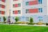 Modern apartment exterior with vibrant facade, lush green lawn, and inviting outdoor seating under blue umbrellas.