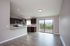 Bright open-plan living space with modern kitchen, sleek countertops, and large sliding glass door leading to a scenic balcony view.
