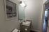 Chic bathroom with elegant vanity, modern lighting, and serene beach artwork, leading to a glimpse of a stylish living area.