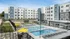 Modern apartment complex with a luxurious outdoor pool, sun loungers, and vibrant yellow umbrellas, surrounded by stylish multi-story buildings.