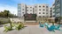 Modern apartment complex exterior with vibrant outdoor seating area, featuring colorful chairs and a cozy fire pit, perfect for relaxation and gatherings under a clear blue sky.