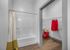 Modern bathroom with sleek white bathtub and spacious walk-in closet featuring stylish red accent decor and wooden flooring.