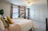 Bright, inviting bedroom with a cozy bed and colorful cushions, enhanced by floral curtains, built-in shelves, and a ceiling fan.