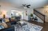 Inviting living room with modern decor, featuring a cozy sectional, vibrant pillows, and a stylish ceiling fan. The open layout extends to the dining area, enhanced by elegant lighting and contemporary furnishings.