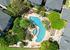 Aerial view of a vibrant apartment complex featuring a large swimming pool, lush green trees, and well-maintained pathways.