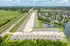 Aerial view of a modern suburban community featuring rows of neatly aligned townhouses, lush green spaces, a beautiful pond, and convenient road access, ideal for tranquil living.