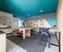 Contemporary workspace with vibrant teal accents, featuring a central wooden table, wall-mounted tools, and sleek black bar stools.