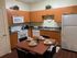 Modern kitchen with sleek wooden cabinets, complete with a dining table set for four, and contemporary appliances including a stove, microwave, and refrigerator.