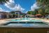 Inviting community pool area with elegant fountains, surrounded by lush greenery and modern amenities under a vibrant blue sky.